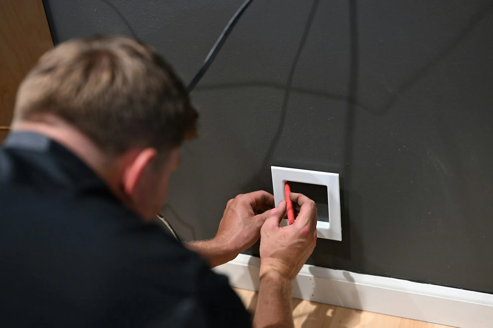 Man fitting a white wall plate over a dark painted wall